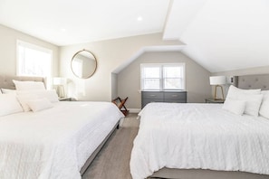 A bedroom with two beds, a dresser, a mirror, and a window.