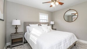 A bedroom with a bed, nightstands, a ceiling fan, a window, and a round mirror.