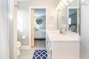 Un baño con inodoro, lavabo, espejo y una cama pequeña al fondo.