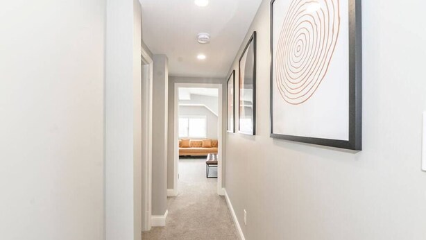 A hallway with framed artwork, a carpeted floor, and a sofa in the background.