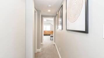 A hallway with framed artwork, a carpeted floor, and a sofa in the background.