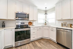 A kitchen with white cabinets, stainless steel appliances, and a wooden floor. - Hot Tub | 7 Beds |  Fire Pit | Patio & Grill (Lexington)