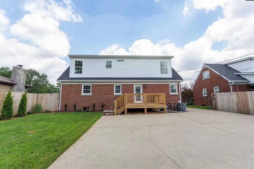 A two-story house with a wooden deck, brick exterior, and a clear sky.