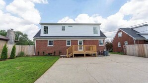 A two-story house with a wooden deck, brick exterior, and a clear sky.