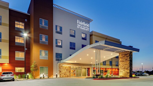 Un hôtel Fairfield Inn & Suites de la chaîne Marriott, doté d’un design moderne, avec une entrée imposante, de nombreux étages et une façade bien éclairée.
