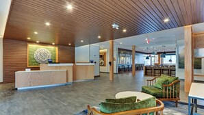 Un hall d’entrée spacieux avec un comptoir d’accueil en bois, des sièges rembourrés de couleur verte et un grand élément décoratif mural.