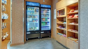 Un espace de vente proposant deux présentoirs réfrigérés étiquetés « Tout ce dont vous avez besoin » et des étagères remplies de collations et de boissons.