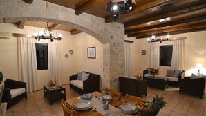 A spacious living area with a stone archway, wooden beams, and a dining table set with plates and a fruit bowl. - Christina II (,)