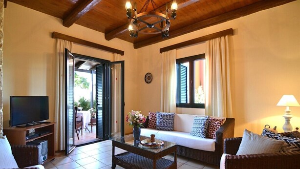 A living room with a television, sofa, coffee table, and a dining area visible through the open door. - Christina II (,)