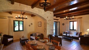 A spacious living area with a dining table set for four, surrounded by wooden furniture and stone walls. - Christina II (,)