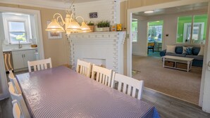 Un coin repas agrémenté d’une cheminée en briques blanches, d’une table recouverte d’une nappe à carreaux et de lampes suspendues.