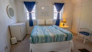 Une chambre à coucher comprenant un lit, une commode, une table de chevet, une chaise et une fenêtre avec des rideaux.
