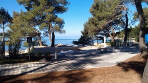 A paved pathway leading to a beach with a wheelchair-accessible sign, surrounded by trees and a clear view of the sea. - STUDIO "GREEN GARDEN" in own SOUTH GARDEN- balcony, 5 minutes walk from the beach, Rovinj  (Rovinj)