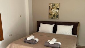 Una cama bien hecha con un edredón color beige, dos almohadas y dos toallas enrolladas sobre la cama.