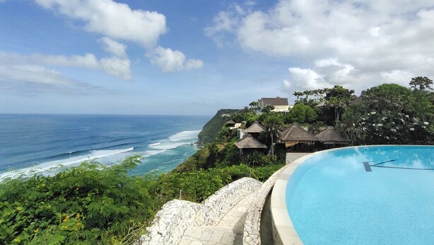 A pool with a view of the ocean and a tropical landscape.