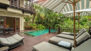 A poolside area with lounge chairs, a wooden deck, and lush tropical plants.