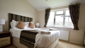 A neatly made bed with a striped blanket, two bedside lamps, a window with curtains, and a radiator.