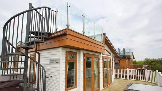 A modern building with a wooden deck, glass railings, and a spiral staircase.