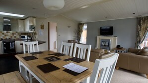 A spacious living area with a wooden dining table, white chairs, a sofa, and a television.