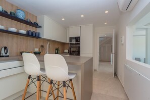 A modern kitchen with white cabinetry, a central island with two white chairs, and a built-in oven.