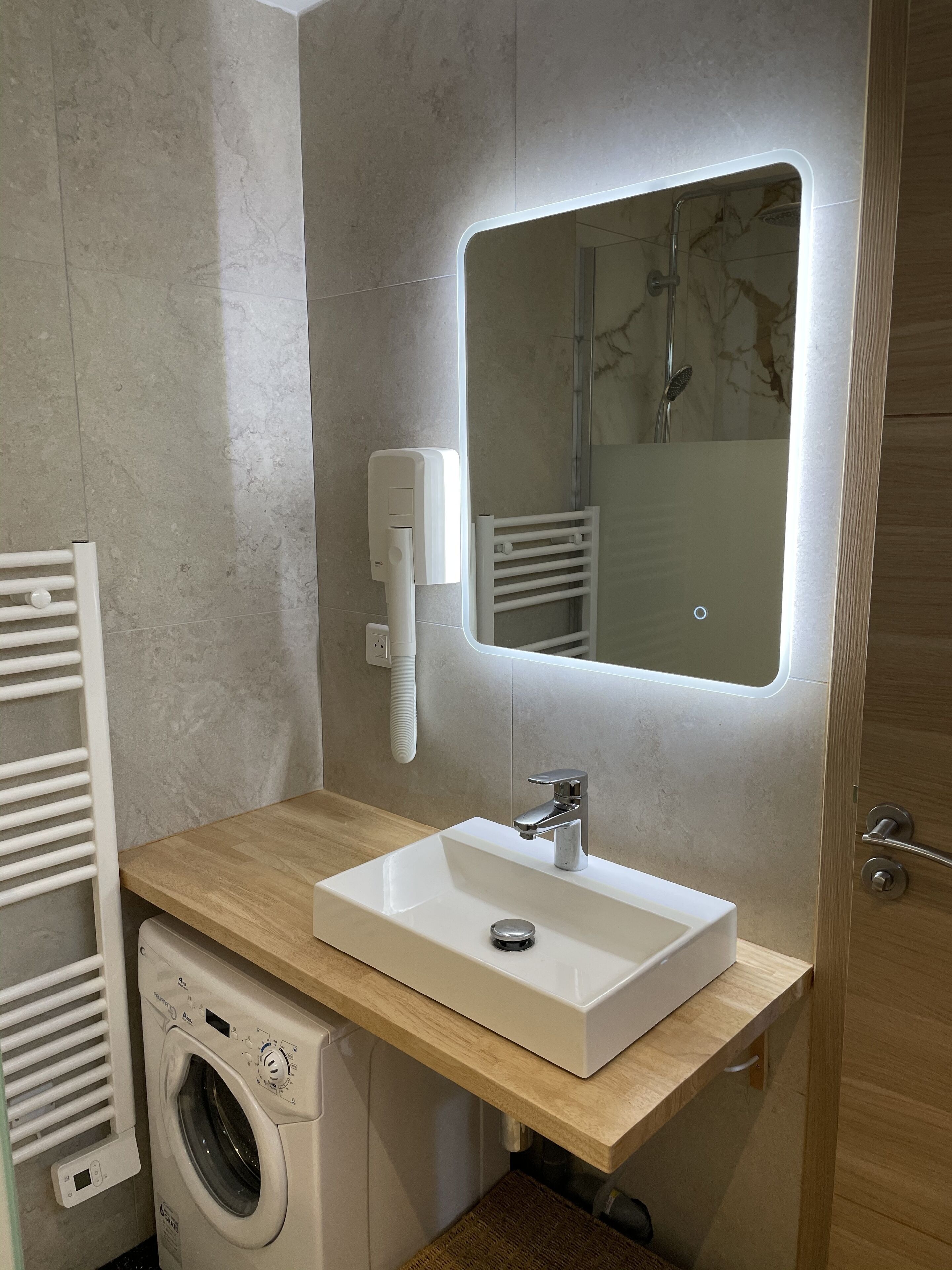 A modern bathroom with a built-in washing machine, a sink with a mirror, and a towel rack.