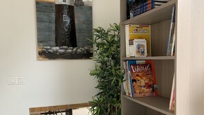 Ein Zimmer mit Bücherregal, einem Leuchtturm-Gemälde, einer Topfpflanze und einem Kamin aus Backsteinen.