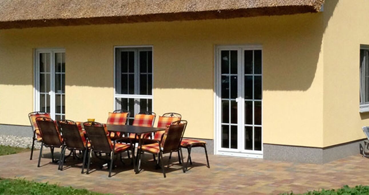 An outdoor patio with a round table and chairs, a thatched roof, and a yellow building facade.