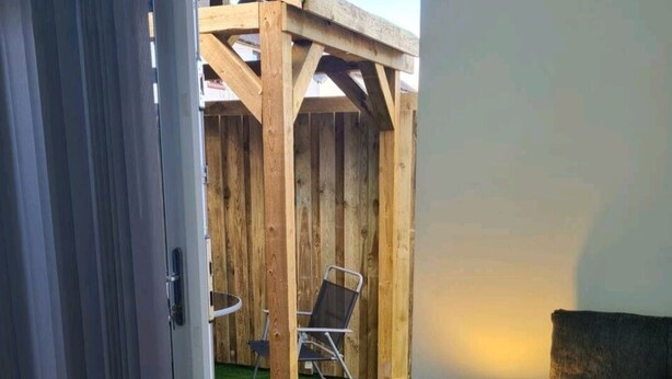 A room with a sliding glass door leading to a wooden deck with a lawn and outdoor furniture. - Charming 1-bed Apartment in Peebles (Peebles)
