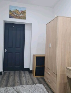 A room with a dark door, a wooden wardrobe, a small wooden cabinet, and a painting on the wall. - Charming 1-bed Apartment in Peebles (Peebles)