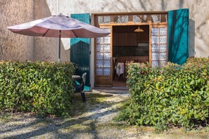 A rustic building with a wooden door and window, a chair outside, and an umbrella. - Le Petit Galla, Country Apartment (PERTUIS)