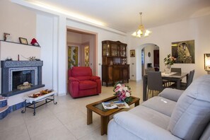 Een woonkamer met een open haard, een rode fauteuil en een eethoek met een tafel en stoelen.