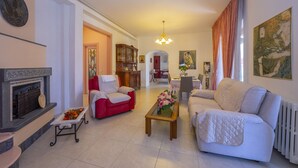 A spacious living room with a fireplace, red and white sofas, a coffee table with flowers, and a dining area in the background. - Villa Clara with Outdoor Jacuzzi few km from the Sea, Pietrasanta, Italy (Pietrasanta)
