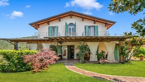 A two-story house with a balcony, a covered porch, and a well-maintained lawn. - Villa Clara with Outdoor Jacuzzi few km from the Sea, Pietrasanta, Italy (Pietrasanta)