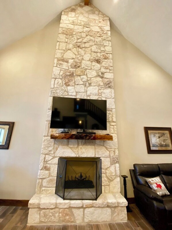 A stone fireplace with a TV mounted above it, a framed picture on the wall, and a leather sofa with a pillow.