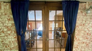 A room with a wooden door, blue curtains, and a brick wall. - Concan River Ranch ~ 1,000' Private Frio River! Mtn. Views, Pet & Polaris OK. (Concan)