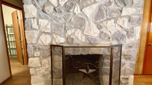 A stone fireplace with a decorative metal screen, set in a room with wooden flooring and a door on the right. - Concan River Ranch ~ 1,000' Private Frio River! Mtn. Views, Pet & Polaris OK. (Concan)