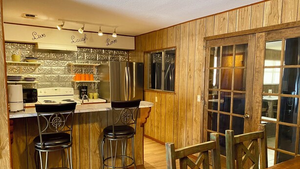 A kitchen with wooden paneling, stainless steel appliances, and bar stools. - Concan River Ranch ~ 1,000' Private Frio River! Mtn. Views, Pet & Polaris OK. (Concan)