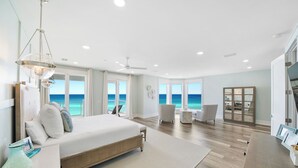 A spacious bedroom with a large bed, a seating area with a view of the ocean, and a built-in cabinet.