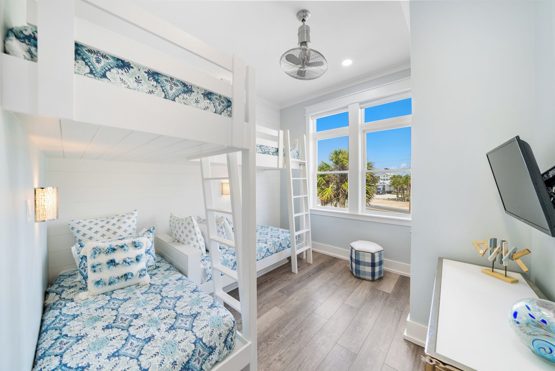 A room with bunk beds, a desk, a chair, a window with a view, and a ceiling fan.
