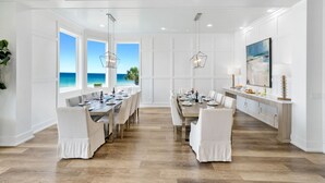 A spacious dining area with a view of the ocean, white walls, and a wooden floor.