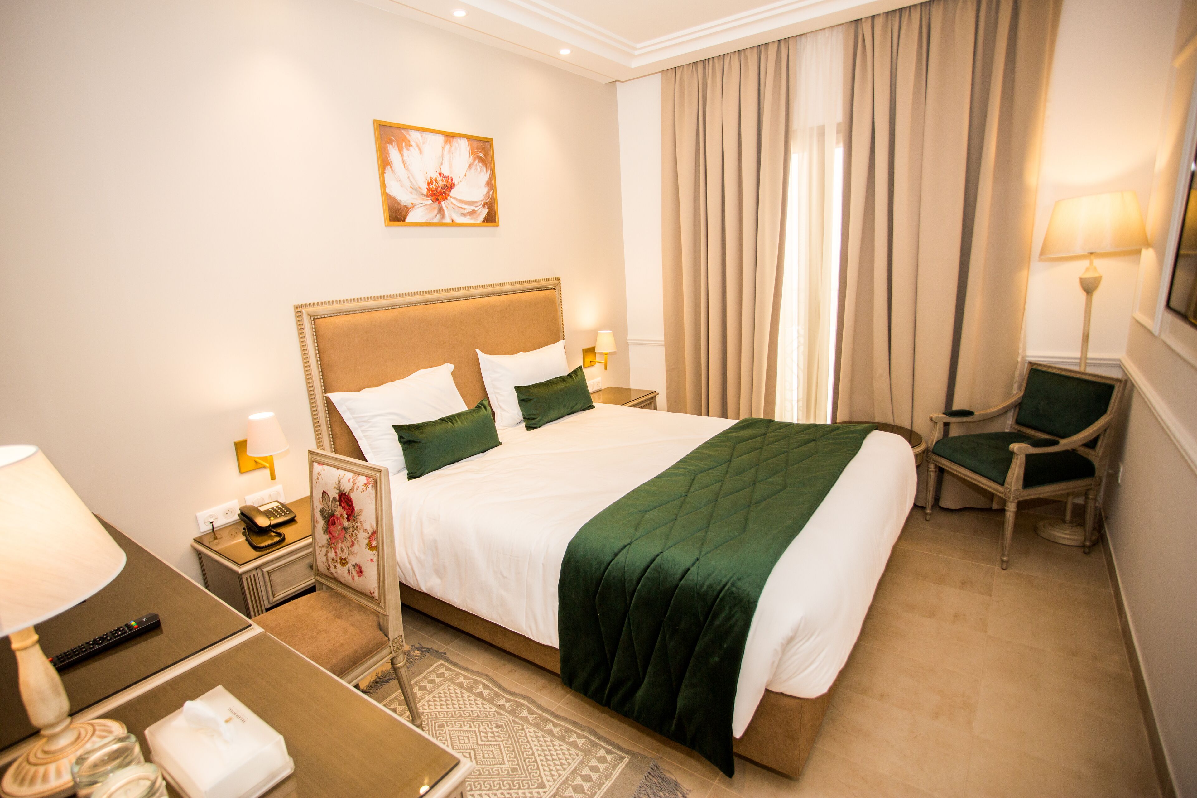 A hotel room with a large bed, a chair, a desk with a lamp, and a telephone.