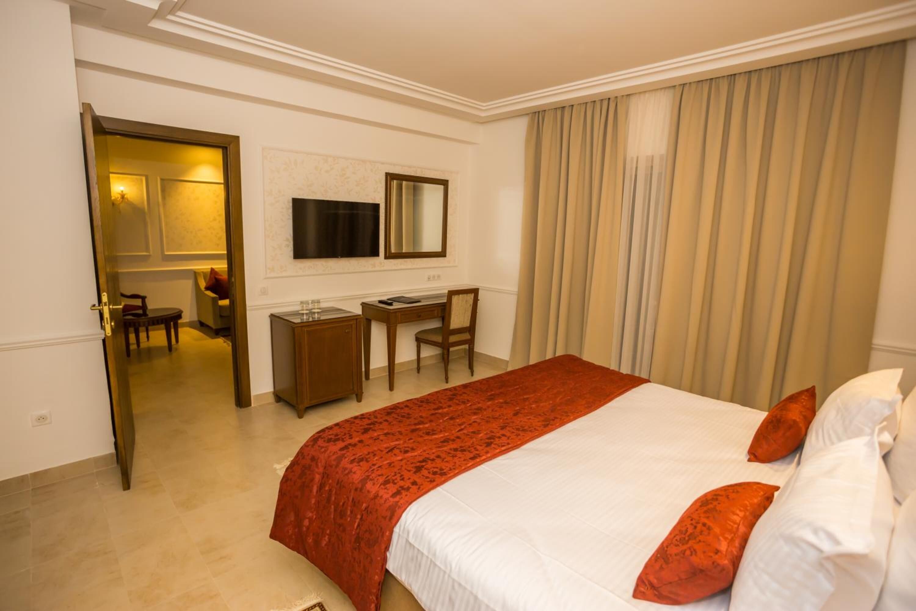 A hotel room with a large bed, a desk, a chair, and a television.