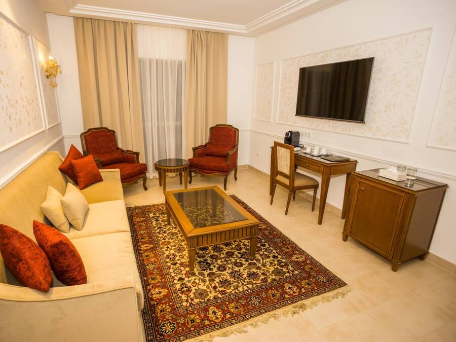 A living room with a sofa, two armchairs, a coffee table, a TV, a small table with a lamp, and a cabinet.