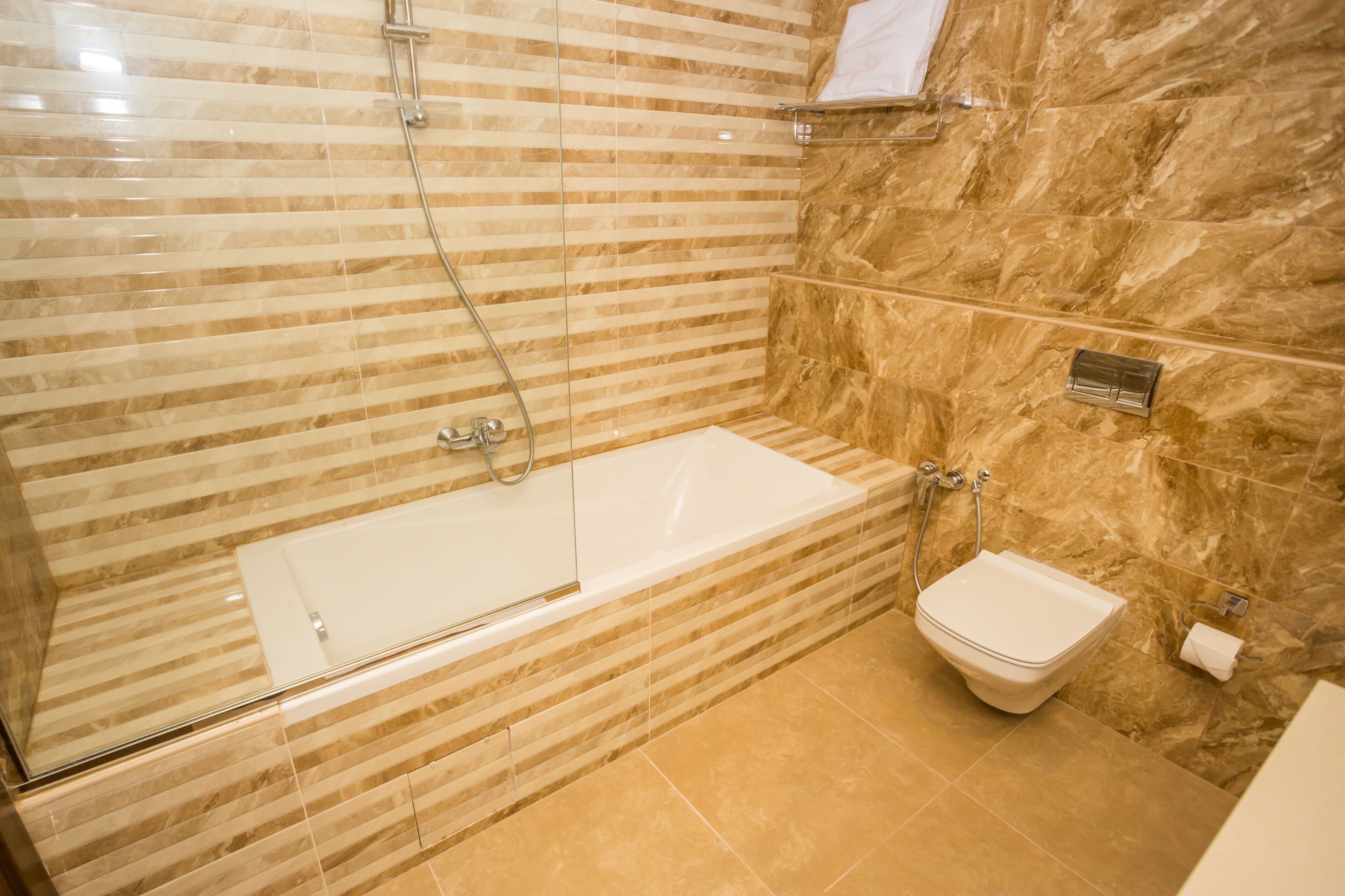 Un baño moderno con bañera de hidromasaje con mampara de vidrio, inodoro y pared de mármol.