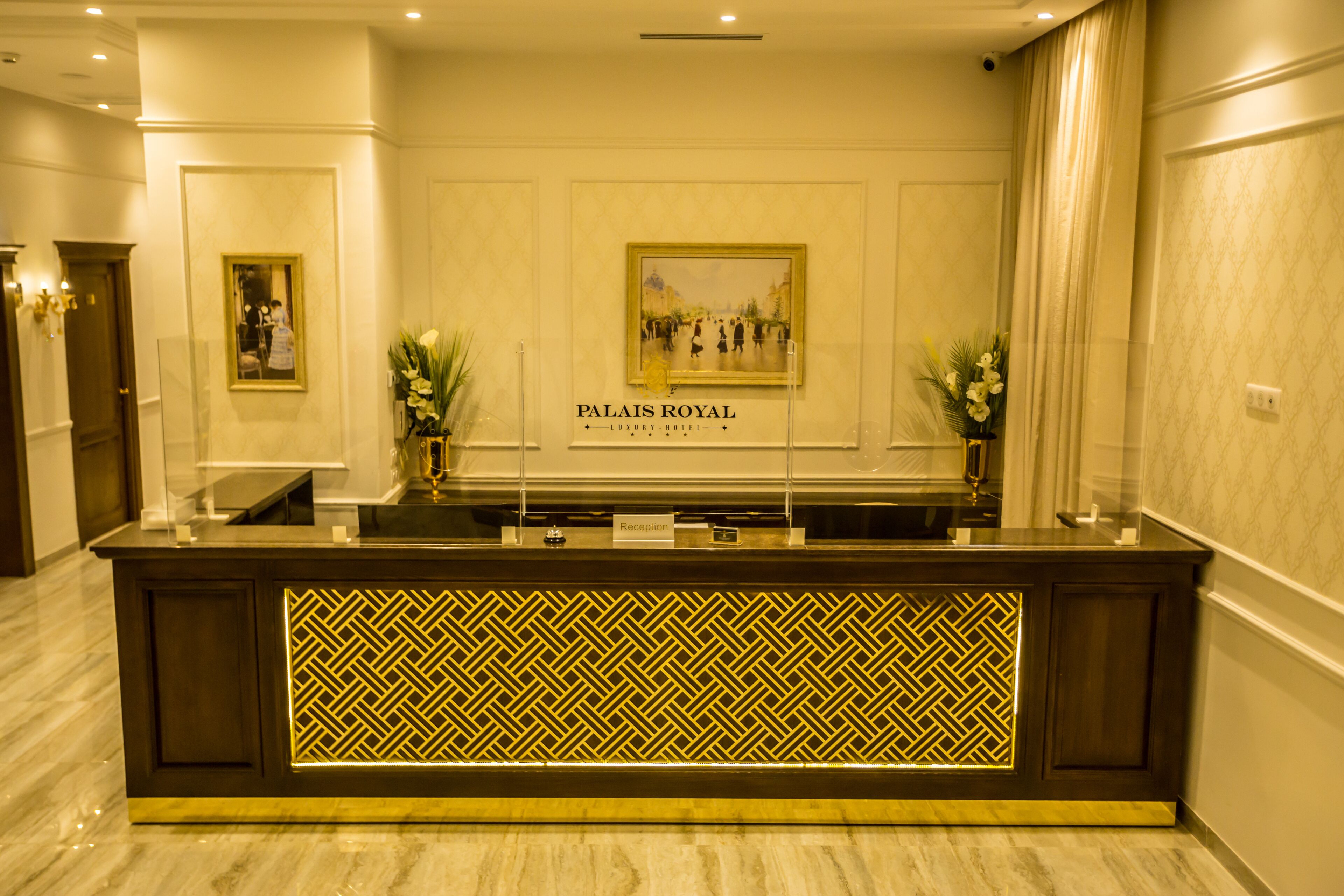Mostrador de recepción en el Hotel Palais Royal Luxury con un muro espejado y obras de arte enmarcadas arriba.