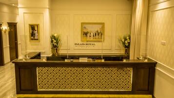 Mostrador de recepción en el Hotel Palais Royal Luxury con un muro espejado y obras de arte enmarcadas arriba.