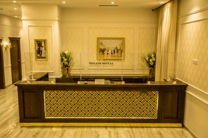 Mostrador de recepción en el Hotel Palais Royal Luxury con un muro espejado y obras de arte enmarcadas arriba.