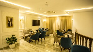 A hotel conference room with a marble floor, a large flat-screen TV, and a dining area with chairs and tables.