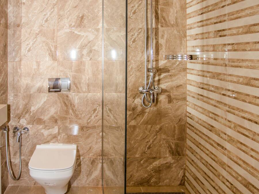 Uma casa de banho moderna com chuveiro em cabine de vidro, sanita e parede de mármore.