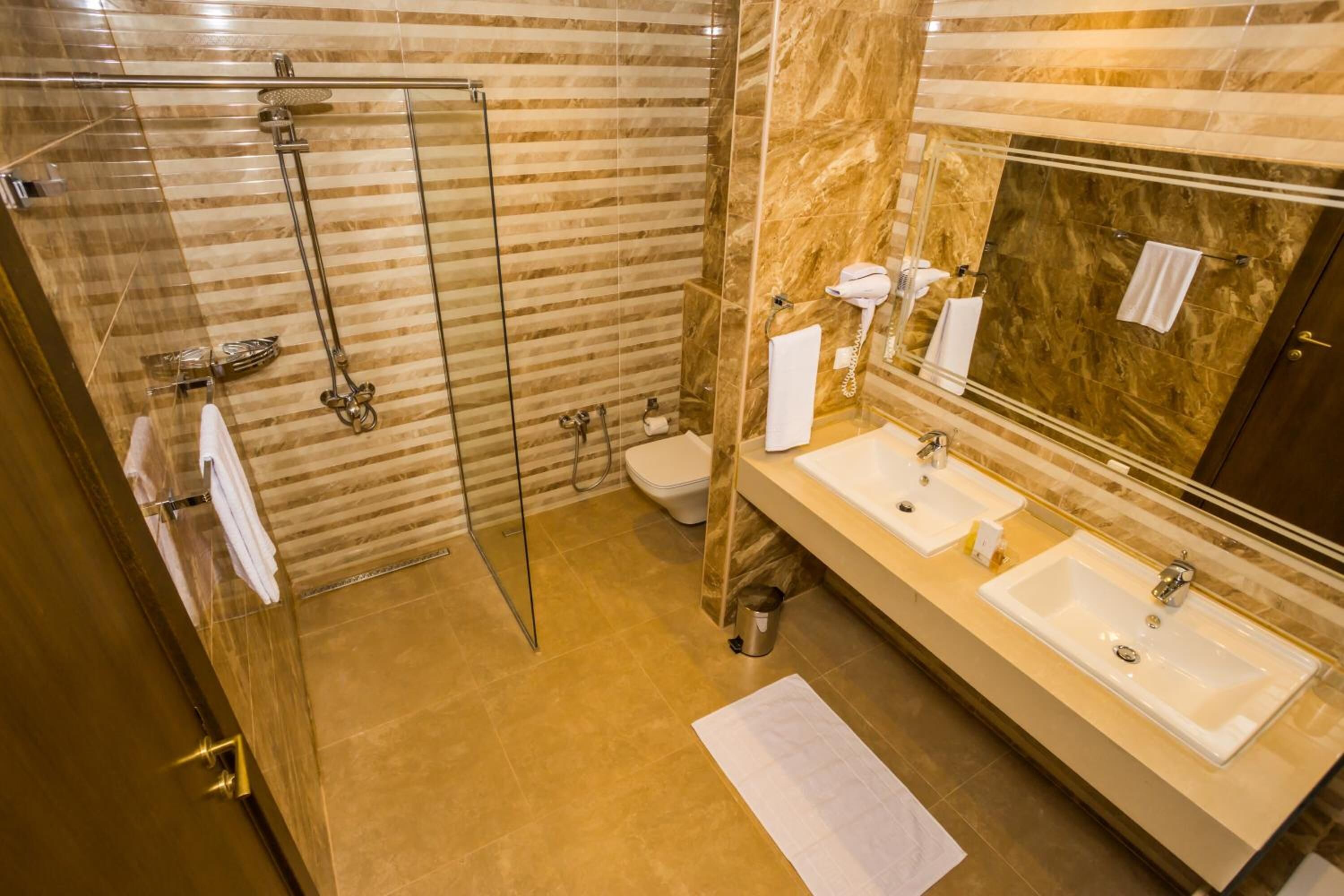 A modern bathroom with a glass-enclosed shower, two sinks, a toilet, and a marble-tiled wall.